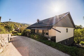 A modern house with a sloped roof, a gravel driveway, and a view of a hillside. - 3 Bedroom Apartment TI&JAZ (Brežice)
