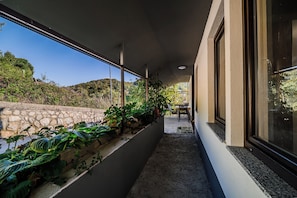 Un couloir avec un mur en pierre d’un côté et une fenêtre de l’autre, qui mène à un espace détente avec une table et des chaises.
