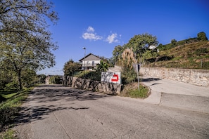 Una strada asfaltata conduce a un edificio con un muro in pietra e un segnale che indica la direzione per 'ARTMA TI & JAZ'.