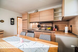 Eine kleine Küche mit Holzausstattung, einem eingebauten Backofen und einer Essecke mit Tisch und Stühlen.