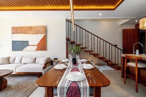 Ein moderner Essbereich mit Holztisch, gedeckt für vier Personen, einer Treppe und einem Wohnzimmer mit Sofa und großem abstrakten Gemälde.