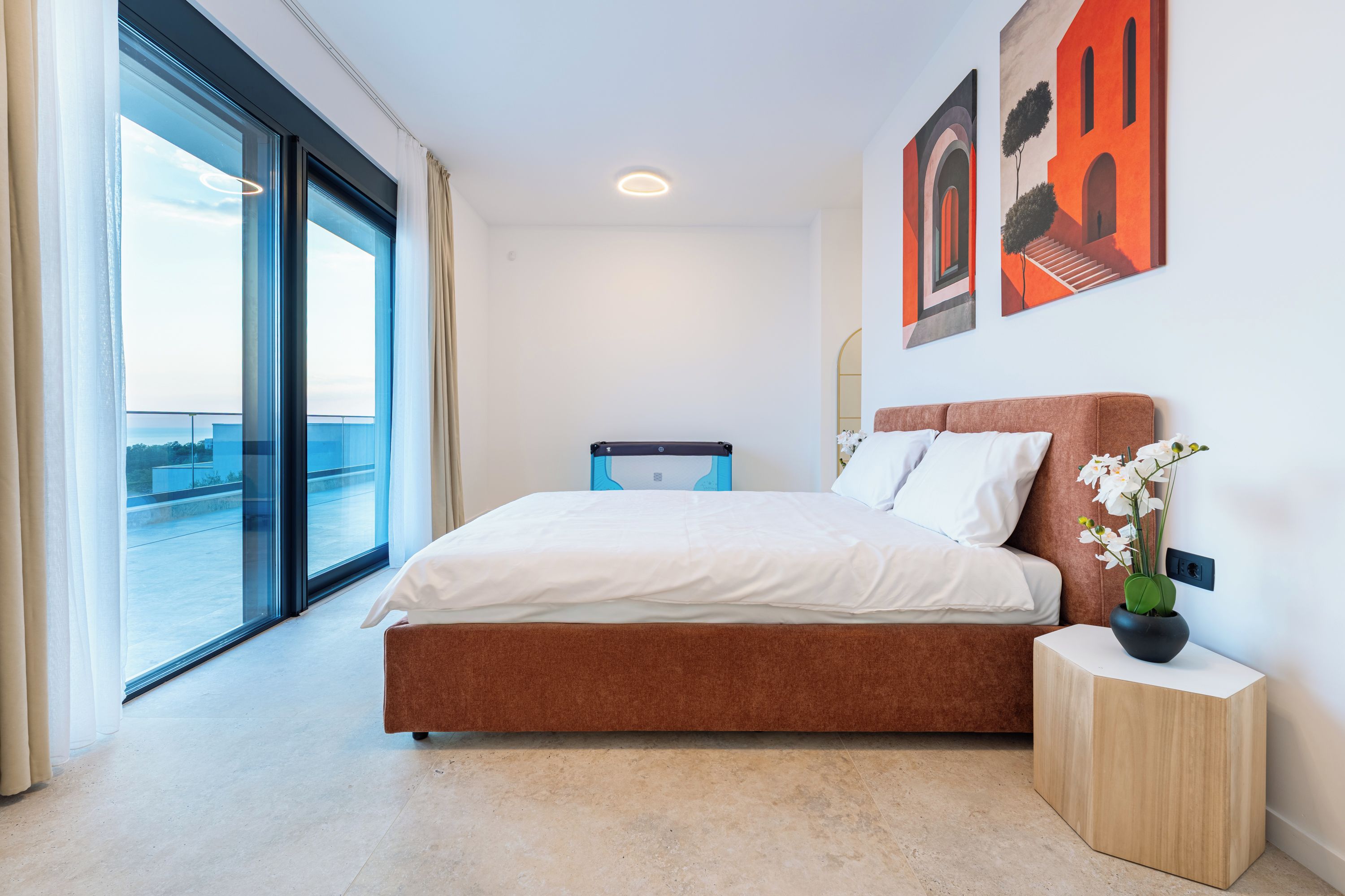 Een hotelkamer met een bed, een nachtkastje, een potplant en kunst aan de muur.