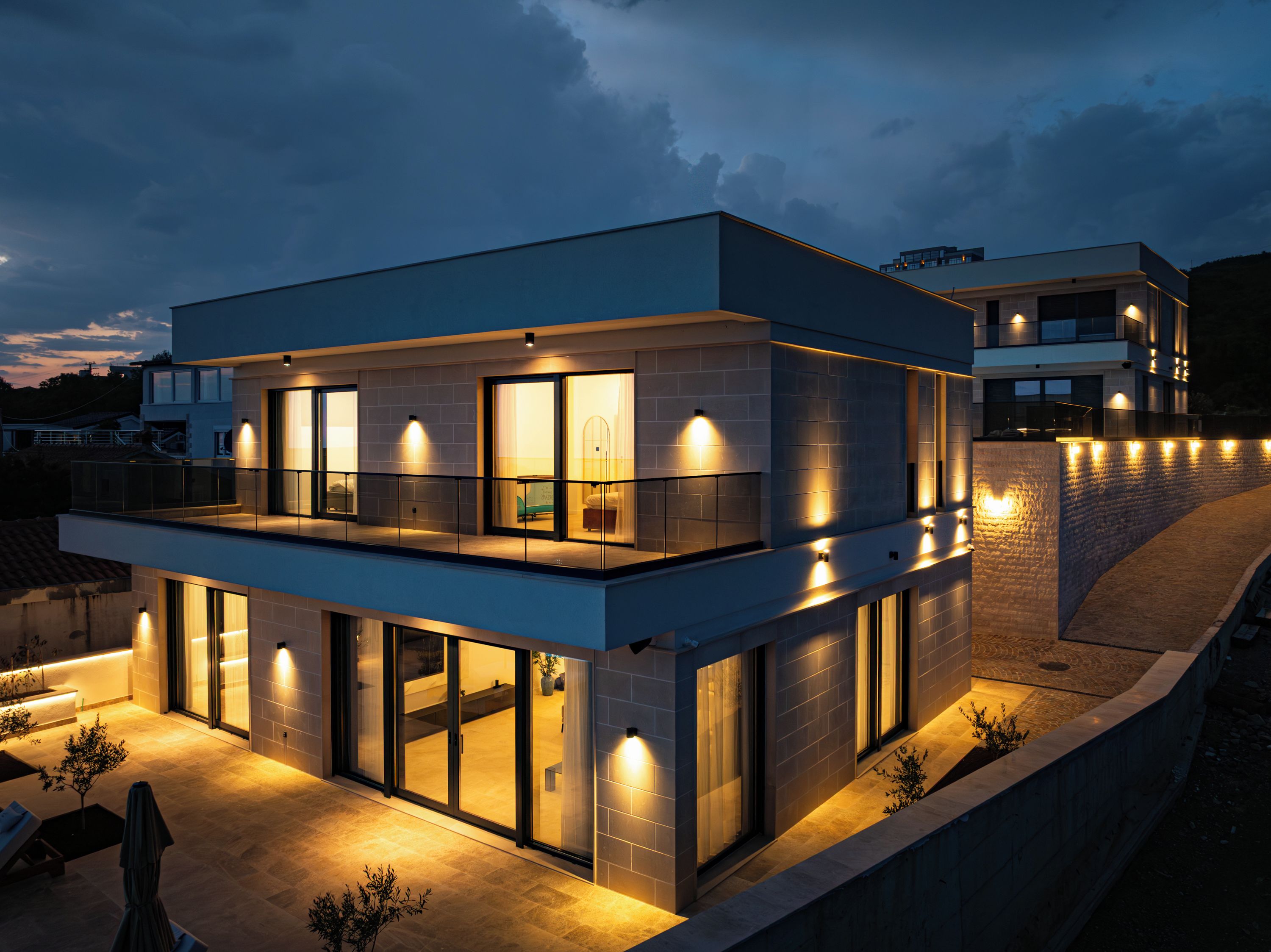 Een modern gebouw met twee verdiepingen, grote glasramen, buitenverlichting en een balkon.