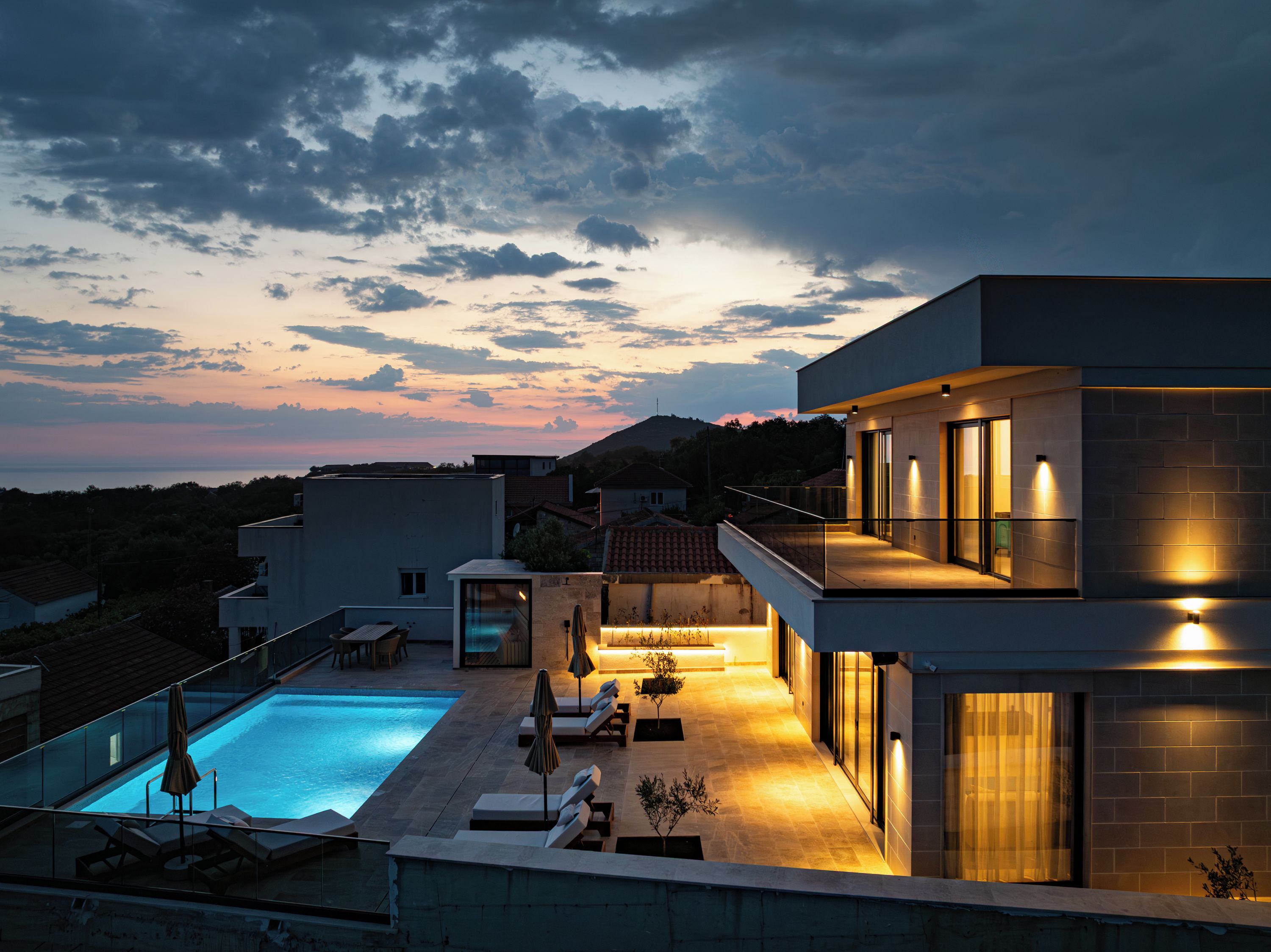 A modern residential building with a swimming pool, outdoor seating, and a balcony overlooking the landscape.