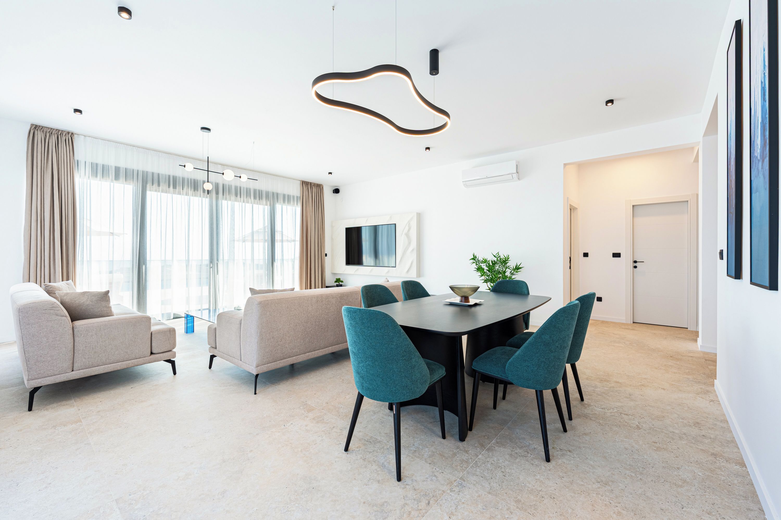 Een moderne woonkamer met een bank, een eettafel met stoelen en een aan de muur bevestigde televisie.