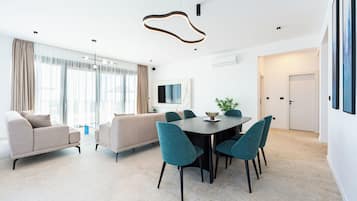 Een moderne woonkamer met een bank, een eettafel met stoelen en een aan de muur bevestigde televisie.