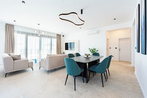 Un salon moderne avec un canapé, une table à manger et des chaises, et un téléviseur fixé au mur.