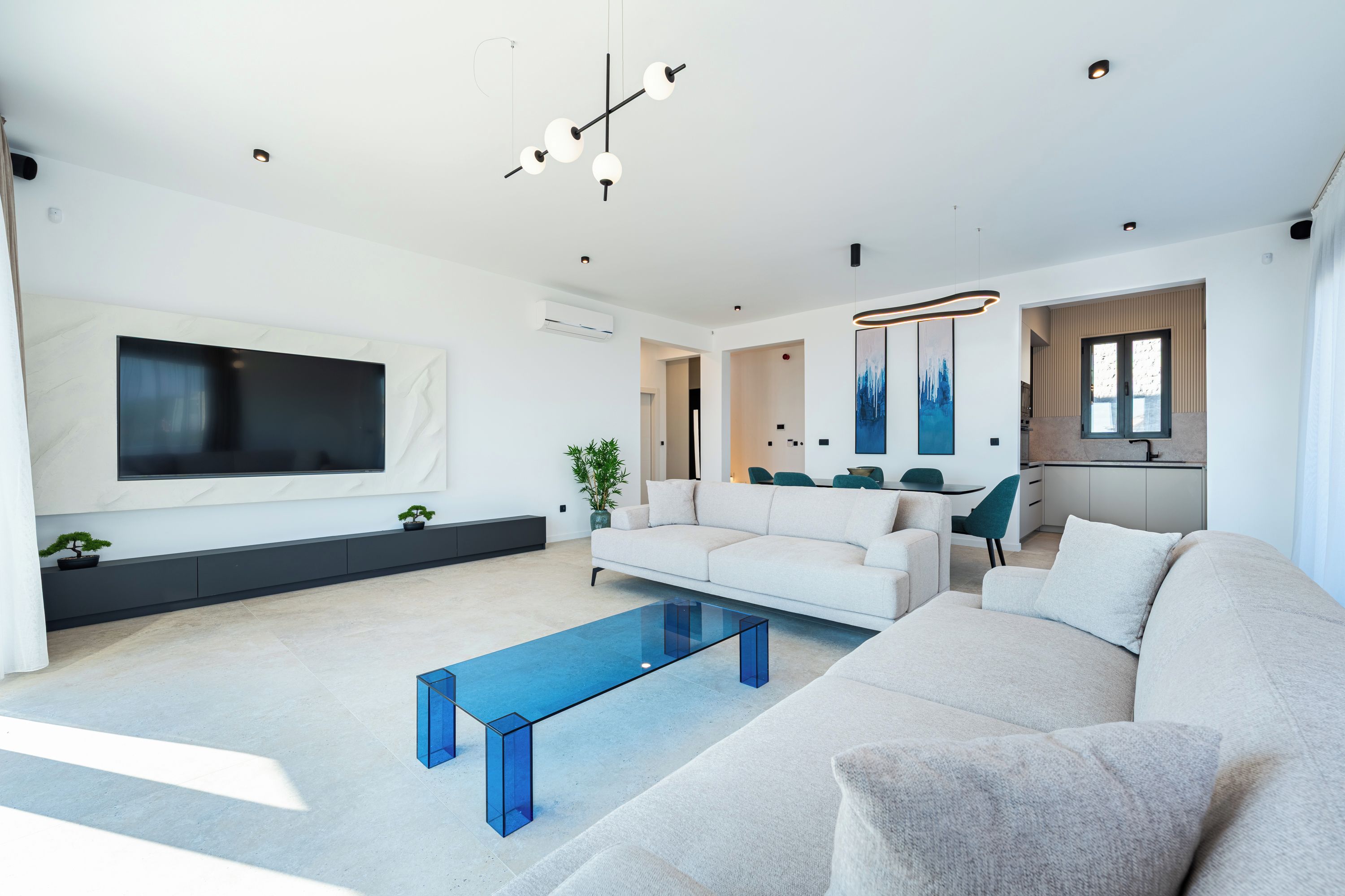 Ein modernes Wohnzimmer mit großem Flachbildfernseher, einer Couch, einem Couchtisch und einem Essbereich mit Stühlen.