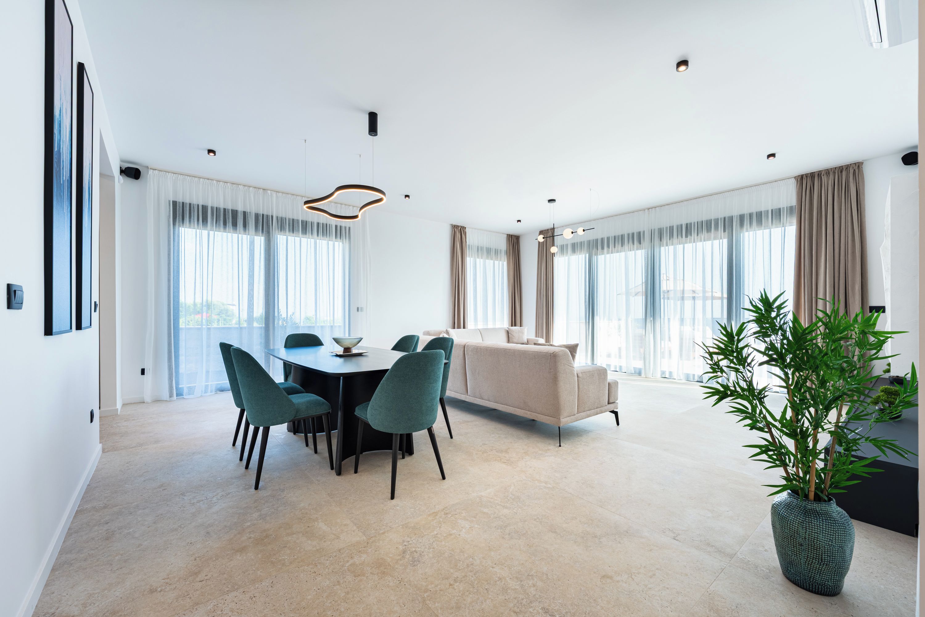 Een moderne woonkamer met een bank, een eettafel met stoelen en een groot raam met gordijnen.