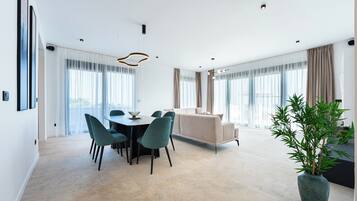 Een moderne woonkamer met een bank, een eettafel met stoelen en een groot raam met gordijnen.