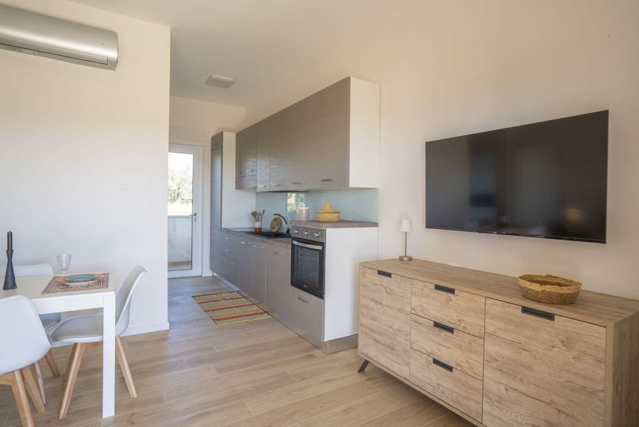 A modern kitchen with a built-in oven, a dining area with a white table and chairs, and a wooden cabinet with a basket.