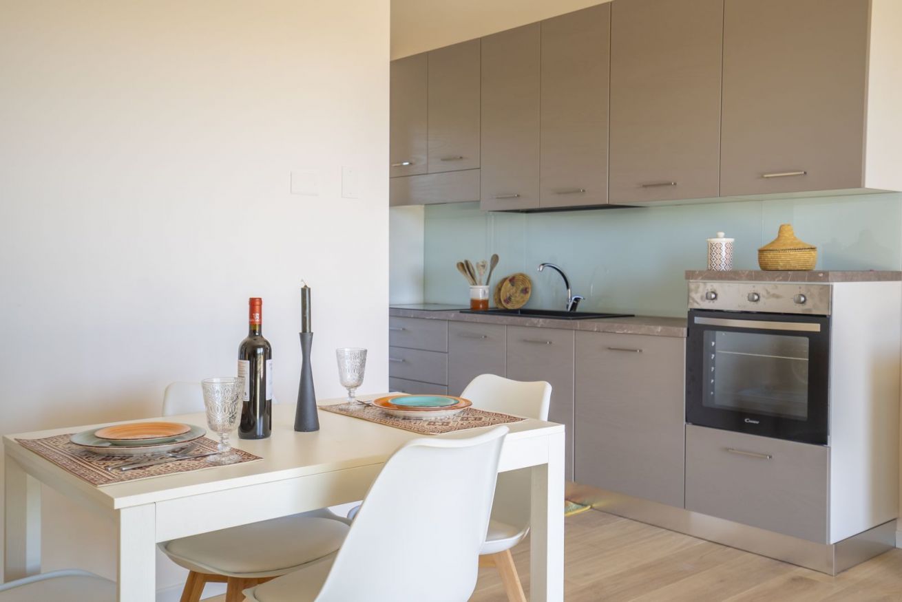 A modern kitchen with a dining table set for two, a built-in oven, and a countertop with kitchen utensils.