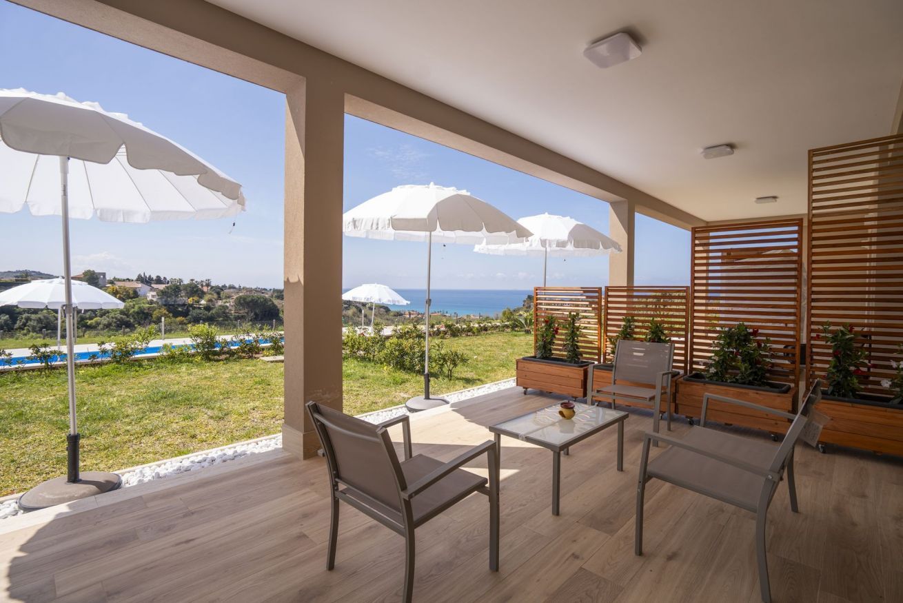 Un ampio balcone con vista sul mare, arredato con sedie e un tavolo, e ombreggiato da grandi ombrelloni.