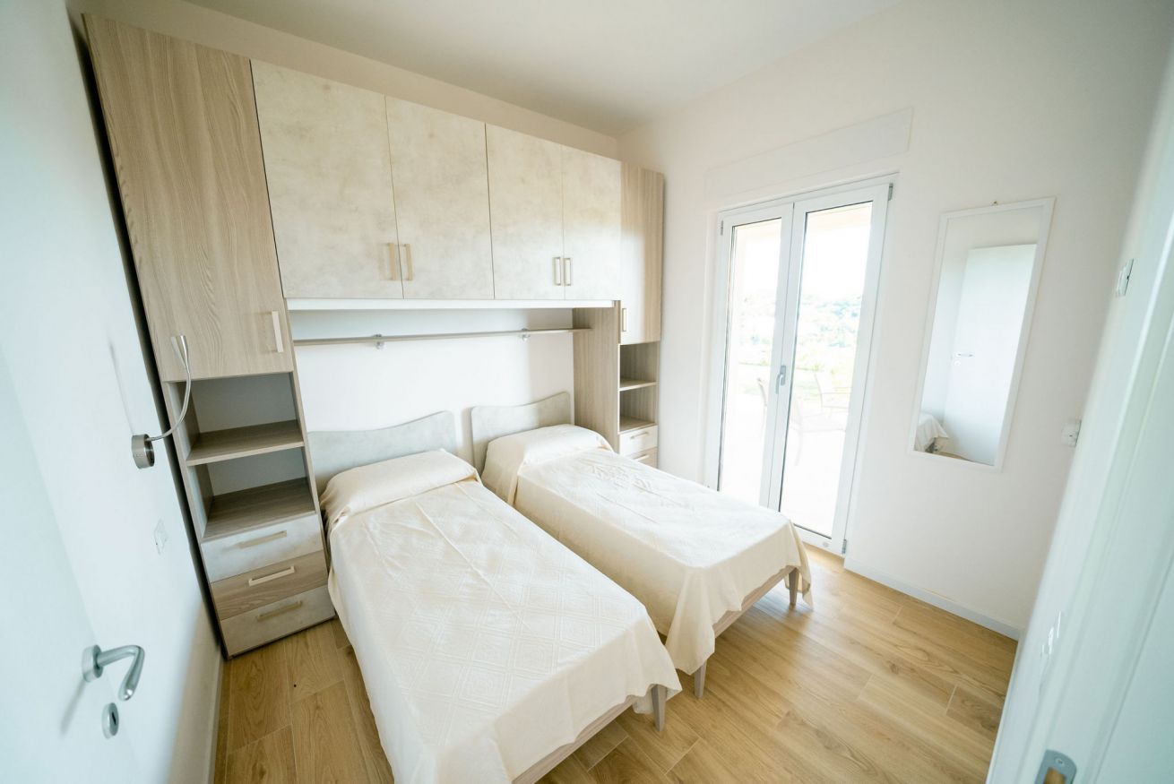 Une chambre avec deux lits, une armoire et une porte coulissante donnant sur un balcon.