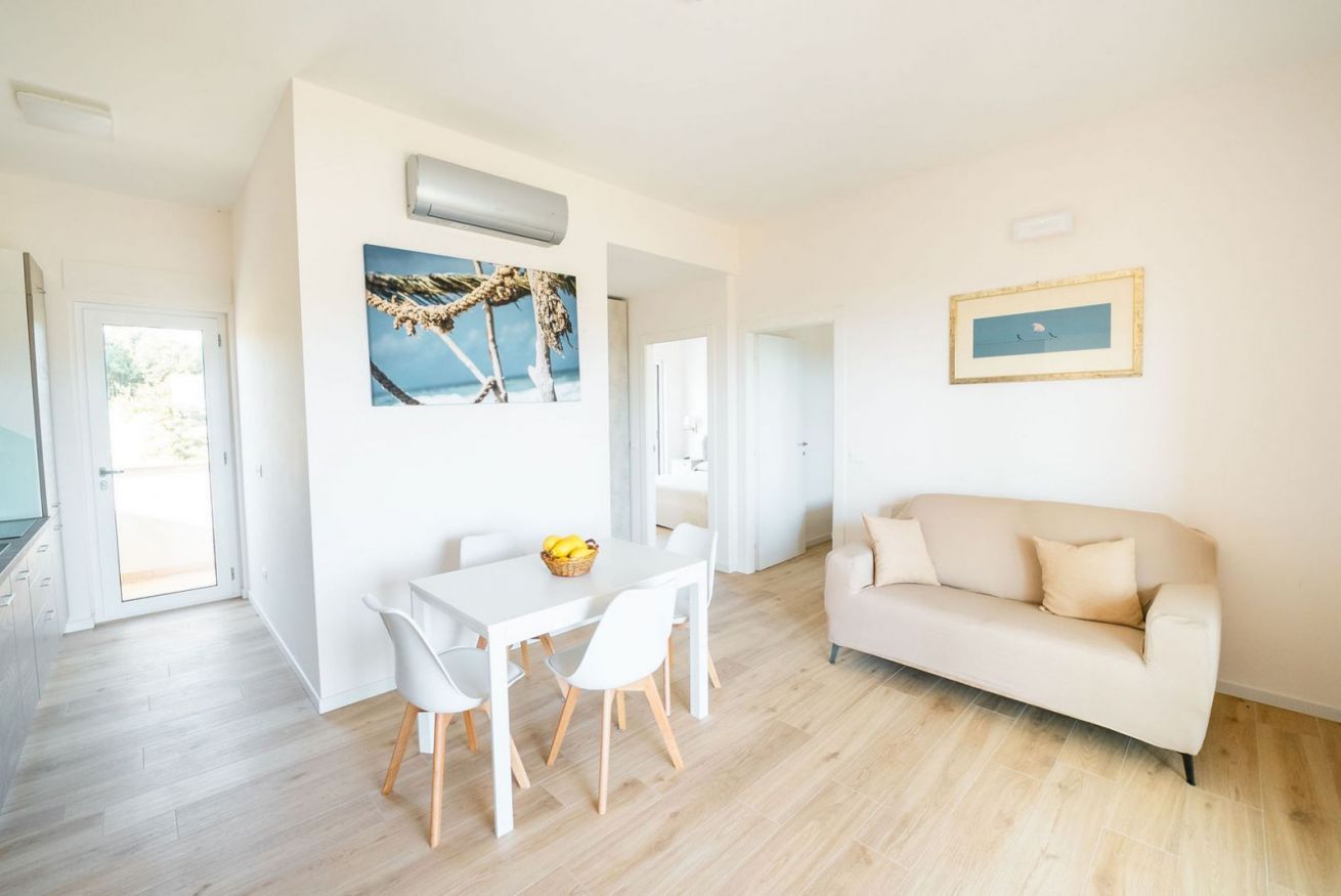 Ein modernes Wohnzimmer mit einem weißen Sofa, einem Esstisch mit Stühlen und einem Bild an der Wand.