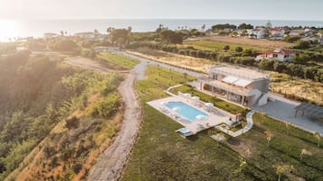 Una villa moderna con piscina, rodeada de un jardín ajardinado y vistas al mar.