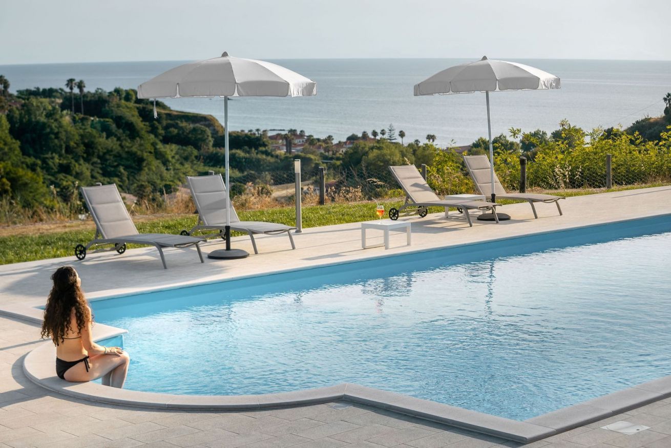 Zona junto a la piscina con sillones de descanso y sombrillas, con vista a una extensión de agua.