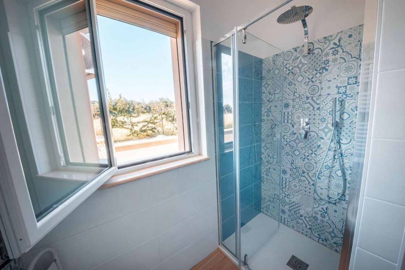 Un baño con ducha, ventana y azulejos con diseño.