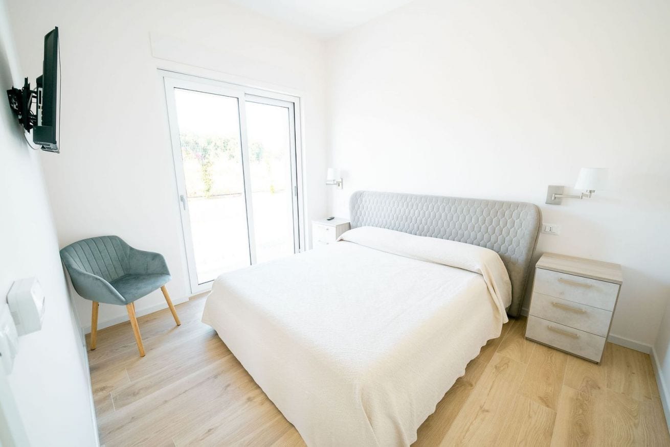 A bedroom with a bed, a chair, a bedside table, and a window.