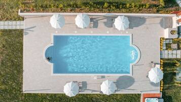 Une vue aérienne d’une piscine rectangulaire, entourée de chaises longues et de parasols, elle-même bordée d’un jardin aménagé.