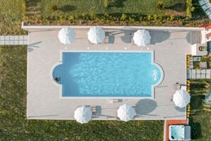 Une vue aérienne d’une piscine rectangulaire, entourée de chaises longues et de parasols, elle-même bordée d’un jardin aménagé.
