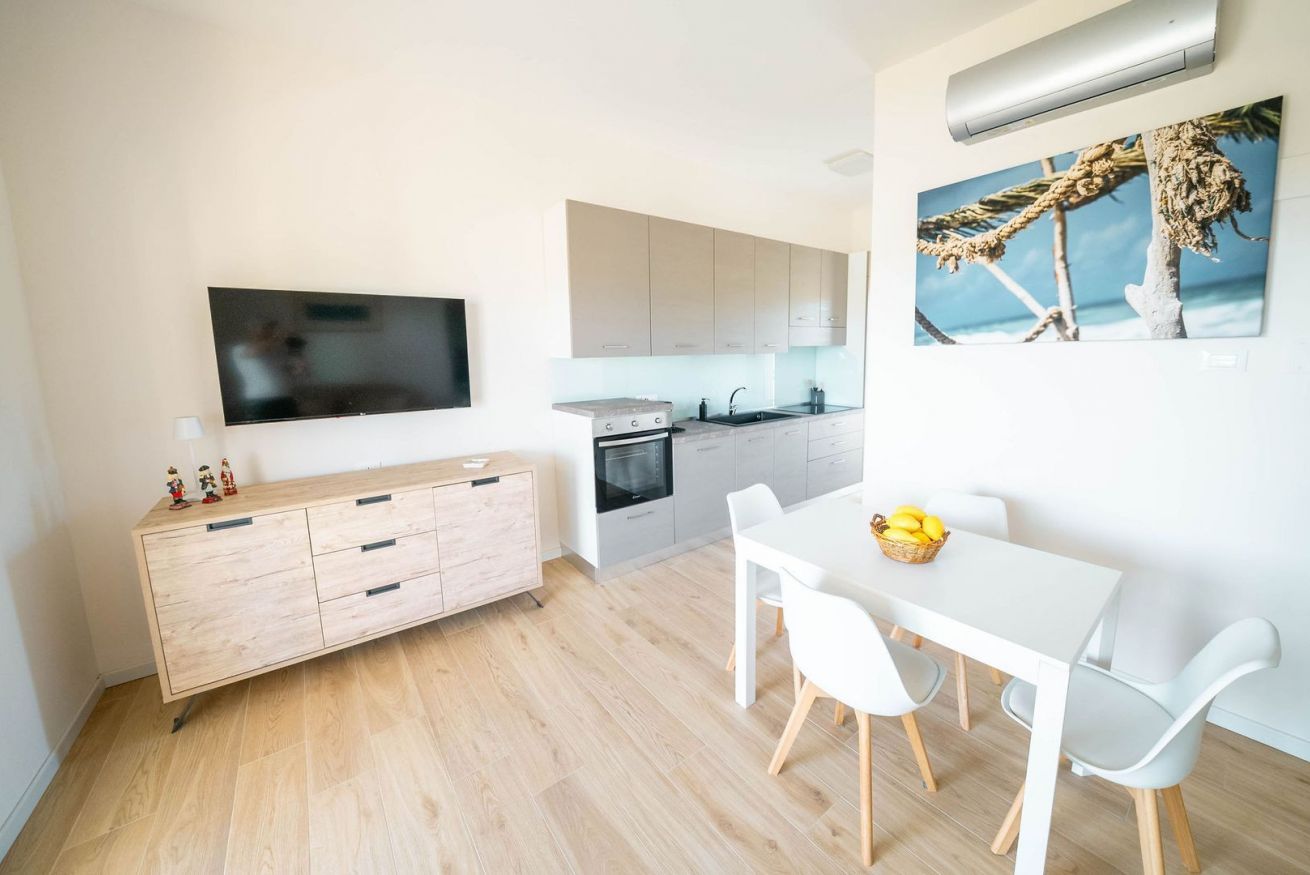 Eine moderne Küche mit Flachbildfernseher, einem Essbereich mit weißem Tisch und Stühlen sowie einem großen Fenster.