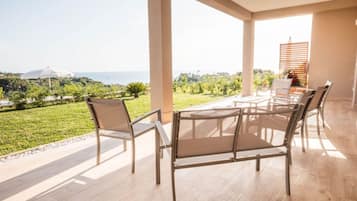 Un espace extérieur aménagé, abrité et doté de sièges, offrant une vue sur la mer et la verdure.