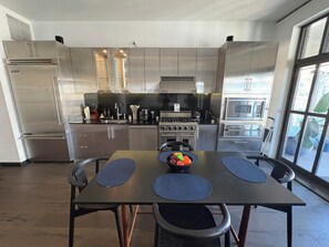 A modern kitchen with stainless steel appliances, a dining table with blue placemats, and a large window providing natural light. - Penthouse Loft in the Grand historic Broadway Hollywood (Los Angeles)