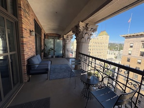 A balcony with a sofa, chairs, and a small table, overlooking a cityscape with buildings and a flag. - Penthouse Loft in the Grand historic Broadway Hollywood (Los Angeles)