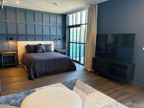 Ein modernes Schlafzimmer mit einem großen Bett, einem Fernseher und Blick ins Freie durch ein großes Fenster.