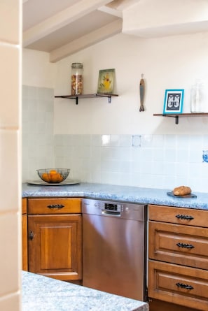 A kitchen with a Bosch dishwasher, wooden cabinets, a marble countertop, and various kitchen items on shelves. - Villa des Landes - familiale - Seignosse (Seignosse)