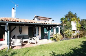 Una casa con porche cubierto, mobiliario de exterior y jardín.