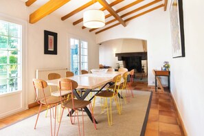 Comedor con una larga mesa y sillas, chimenea y vista a la vegetación exterior.
