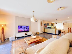 A modern living room with a flat-screen TV, a wooden coffee table, a sofa, and a kitchen in the background. - Cosy, a tropical haven steps from the beach (Saint-Martin)