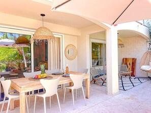 An outdoor dining area with a wooden table and white chairs, a hanging wicker chair, and a woven ceiling light. - Cosy, a tropical haven steps from the beach (Saint-Martin)