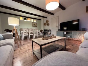 A modern living room with a wooden coffee table, white sofas, a dining area with white chairs, a television, and pendant lighting. - House Strandherz, Part Port (Utersum)