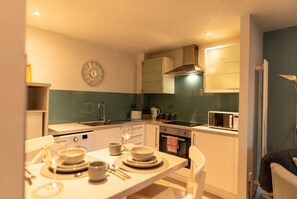 A modern kitchen with a dining table set for two, a microwave, and a stove. - Ground-Floor 2-Bed Sleeps 4 · Parking · Walk to Cardiff Bay (Cardiff)