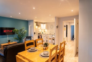 A modern kitchen with white cabinets and a dining area with a wooden table set for four. - Ground-Floor 2-Bed Sleeps 4 · Parking · Walk to Cardiff Bay (Cardiff)