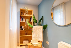 A bathroom with a wooden shelf holding books and decorative items, a white towel, and a mirror on the wall. - Ground-Floor 2-Bed Sleeps 4 · Parking · Walk to Cardiff Bay (Cardiff)