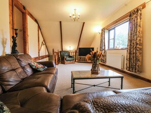 A living room with a brown leather sofa, a wooden coffee table, a green armchair, and a TV in the background. - The Barn (Tamworth)