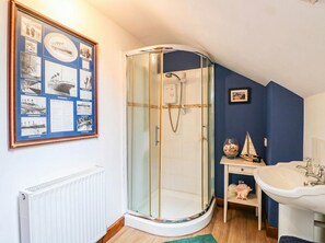 A bathroom with a glass-enclosed shower, a framed nautical-themed bulletin board, a white radiator, and a wooden shelf with decorative items. - The Barn (Tamworth)