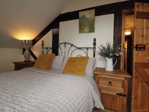 A bedroom with a bed, nightstands, a lamp, a painting, and a wooden door. - The Barn (Tamworth)