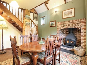 A dining area with a wooden table and chairs, a fireplace, and a staircase. - The Barn (Tamworth)