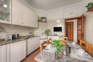 Een moderne keuken met witte kasten, een granieten aanrecht, een eettafel voor vier personen en een televisie boven het aanrecht.