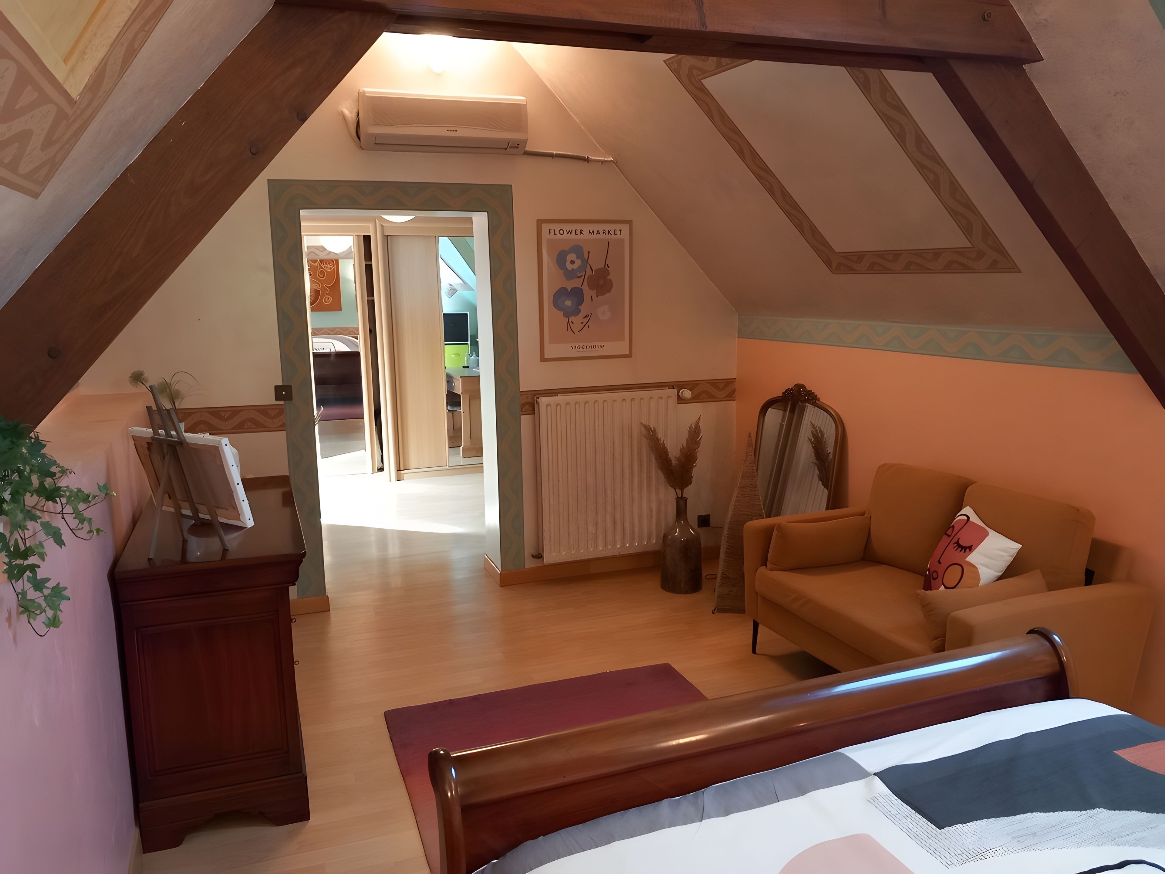 Een slaapkamer met een schuine kap, een bed, een slaapbank, een dressoir en een spiegel.