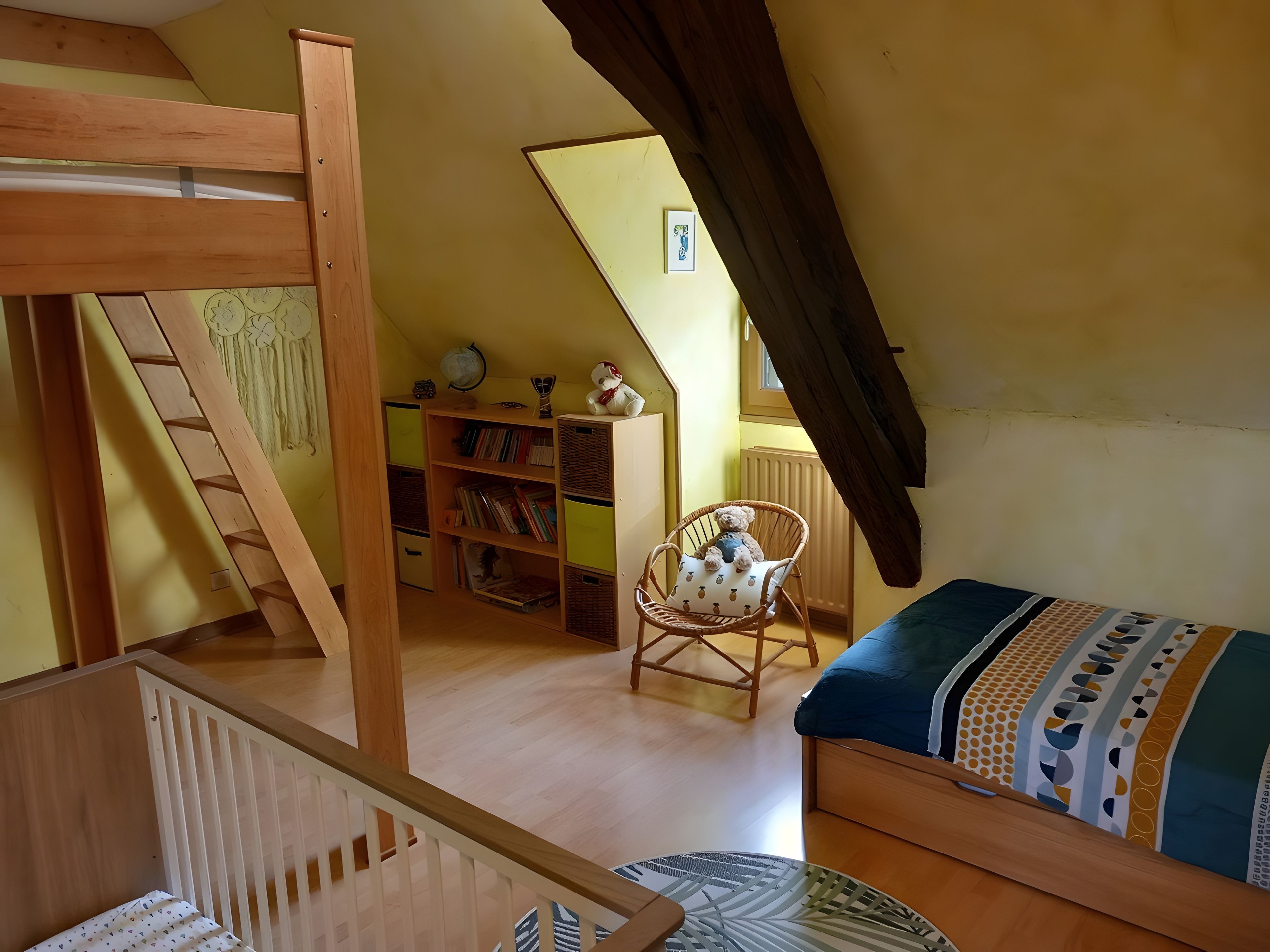 A cozy attic room with a bunk bed, a bookshelf, a chair, and a small table.