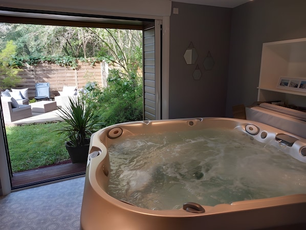 A spa area with a hot tub, a patio with outdoor furniture, and a view of a garden.