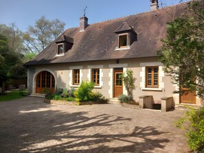 Een tweelaags huis met een bakstenen schoorsteen, een groot rondboogvenster en een geplaveid pad.