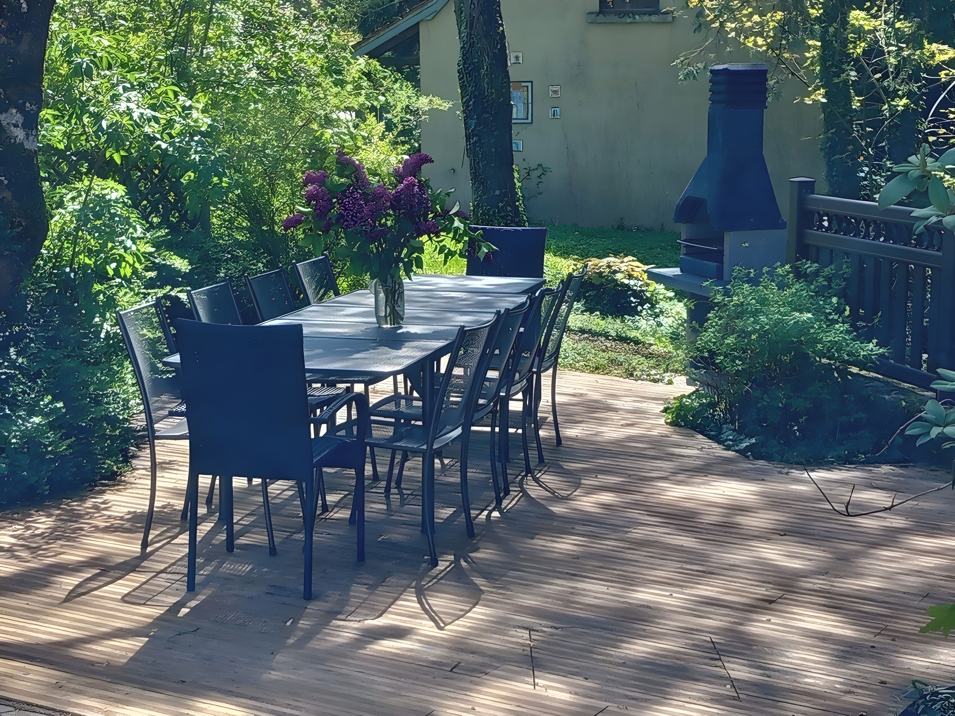 A wooden deck with a table and chairs, surrounded by lush greenery and a garden.