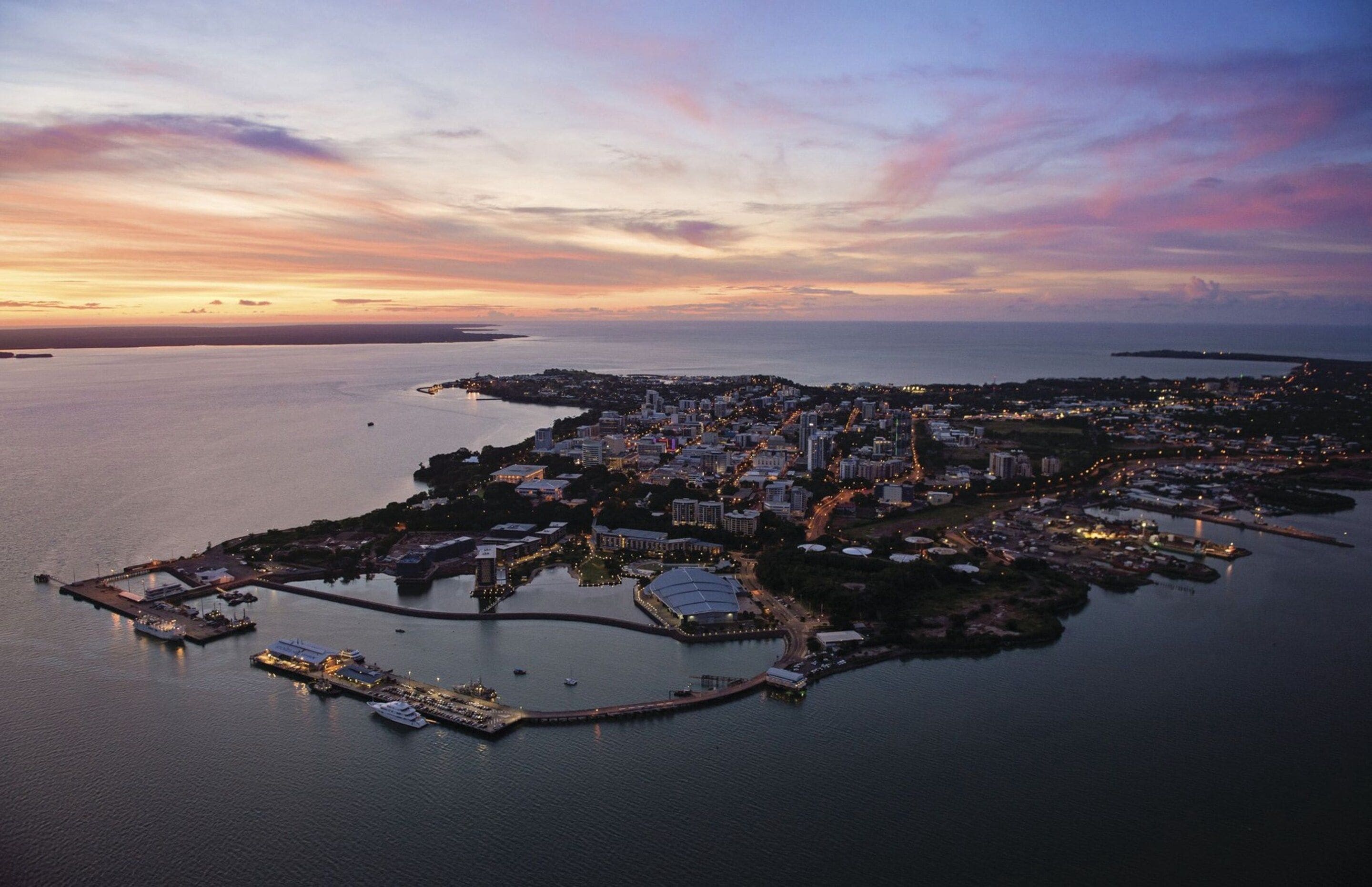 Vista aérea de una ciudad costera con un puerto deportivo, edificios y una extensa masa de agua.
